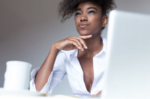Stylish dark-skinned woman food blogger with curly haircut publishing new posts on social networks, using laptop